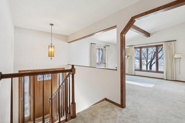 hallway with carpet, baseboards, beamed ceiling, and an upstairs landing