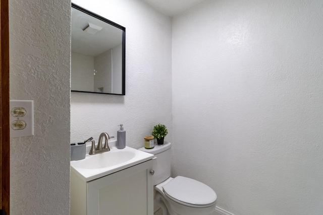 half bathroom featuring toilet, a textured wall, and vanity