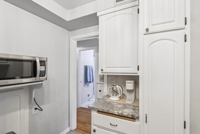 kitchen with light wood finished floors, stainless steel microwave, backsplash, and white cabinetry