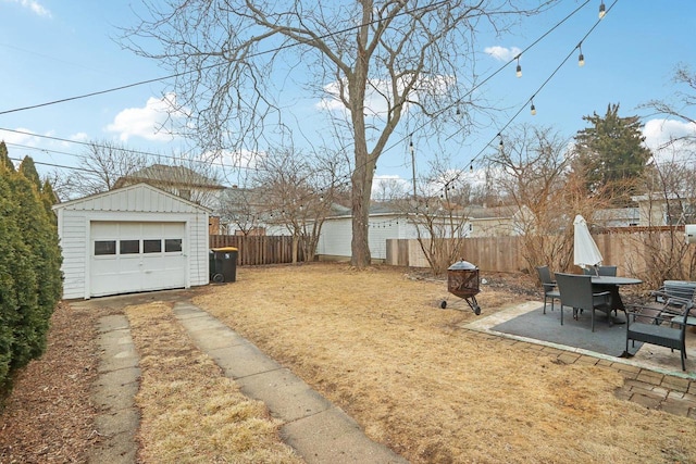 view of yard with a garage, driveway, a fenced backyard, an outdoor structure, and a patio area