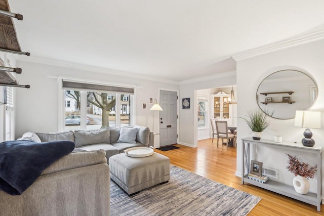 living area featuring baseboards, ornamental molding, light wood-type flooring, and an inviting chandelier