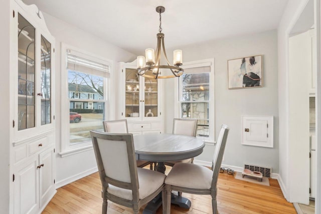 dining room featuring light wood-type flooring, visible vents, a notable chandelier, and baseboards