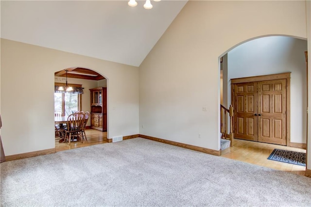 carpeted empty room featuring arched walkways, high vaulted ceiling, visible vents, and baseboards