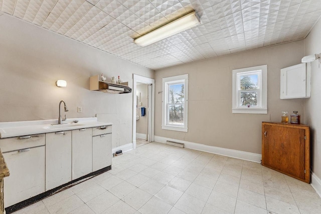 kitchen featuring light countertops, a sink, baseboards, and white cabinetry