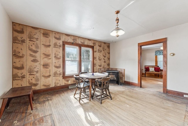 dining area featuring a wood stove, light wood-style flooring, and baseboards