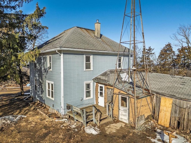 rear view of house with roof with shingles and a chimney