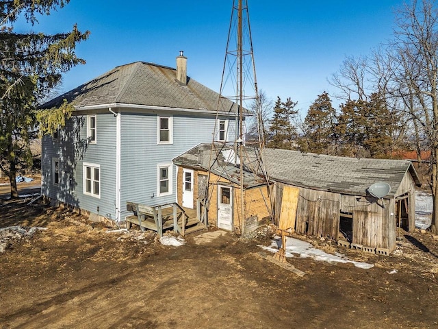 rear view of property featuring a shingled roof and a chimney