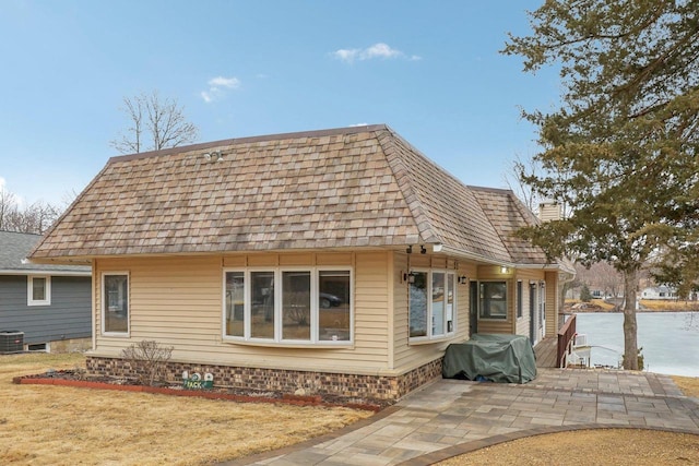 view of front facade with a patio area, a chimney, central AC, and roof with shingles