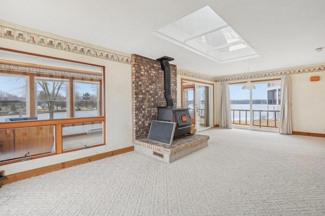 unfurnished living room with a skylight, a wood stove, carpet flooring, and baseboards