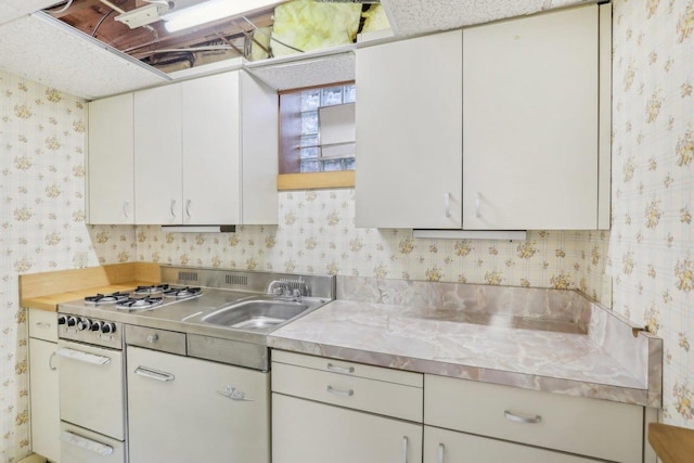 kitchen with stainless steel counters, white cabinets, a sink, white range with gas stovetop, and wallpapered walls