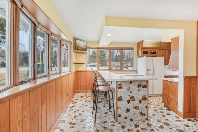 kitchen with a wainscoted wall, wooden walls, white fridge with ice dispenser, and a sink