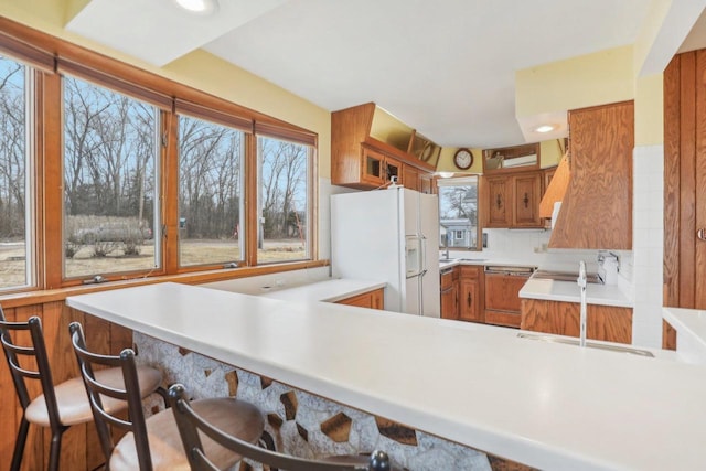 kitchen featuring brown cabinetry, paneled dishwasher, a peninsula, light countertops, and white fridge with ice dispenser