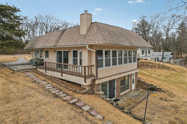 back of property with a shingled roof, a yard, a wooden deck, a chimney, and a patio area