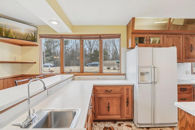 kitchen with white fridge with ice dispenser, light countertops, brown cabinetry, and a sink