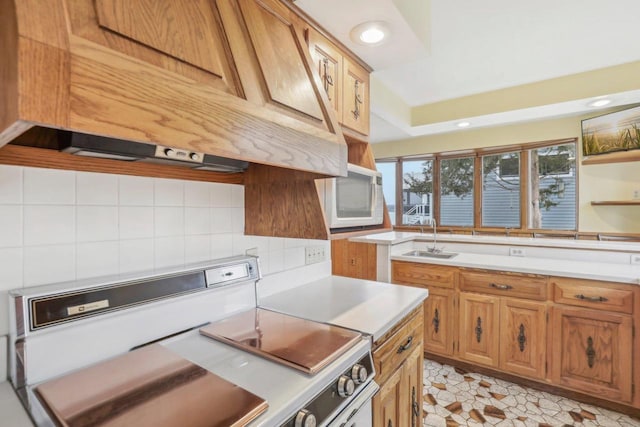 kitchen with custom exhaust hood, light countertops, decorative backsplash, white microwave, and a sink