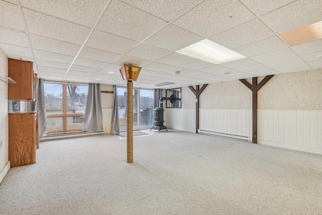 below grade area with a wainscoted wall, a drop ceiling, and carpet flooring