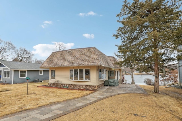 view of front facade featuring central AC unit, mansard roof, a patio, roof with shingles, and a front lawn