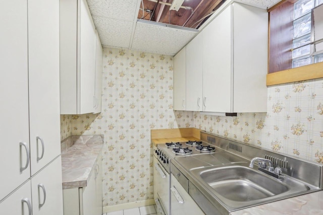 kitchen featuring a sink, white cabinetry, light countertops, gas range oven, and wallpapered walls