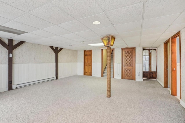 finished below grade area featuring a paneled ceiling, carpet, a baseboard radiator, and wainscoting