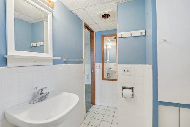 bathroom featuring wainscoting, tile patterned floors, a sink, a paneled ceiling, and tile walls