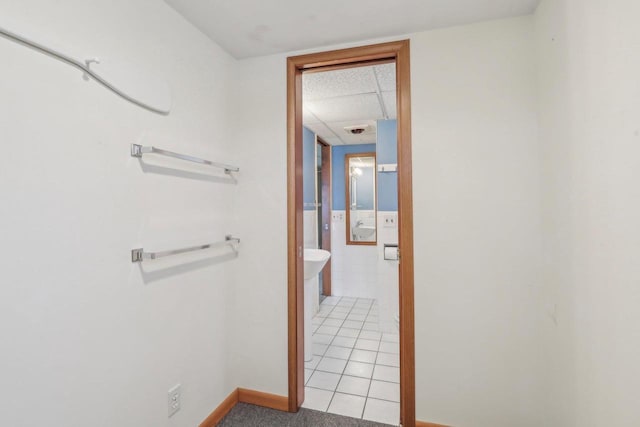 corridor with light tile patterned floors, a drop ceiling, and baseboards