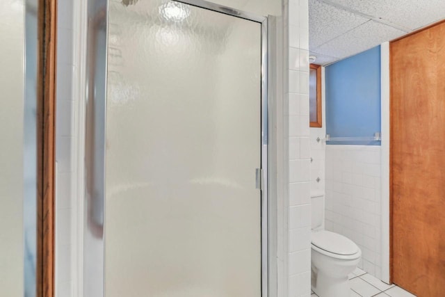 bathroom featuring a drop ceiling, tile patterned flooring, toilet, tile walls, and a shower stall