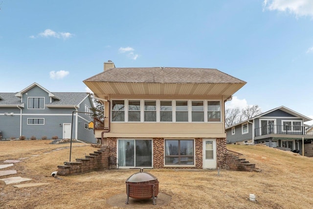 back of house with a fire pit, brick siding, a shingled roof, stairs, and a chimney