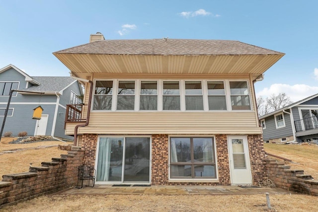 back of property featuring brick siding and roof with shingles