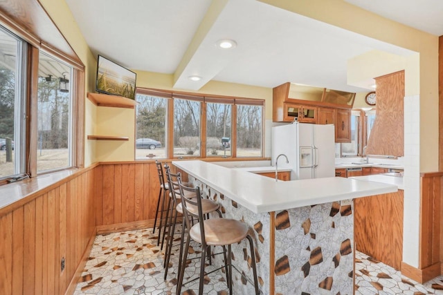 kitchen with a wainscoted wall, white fridge with ice dispenser, a kitchen breakfast bar, and wood walls