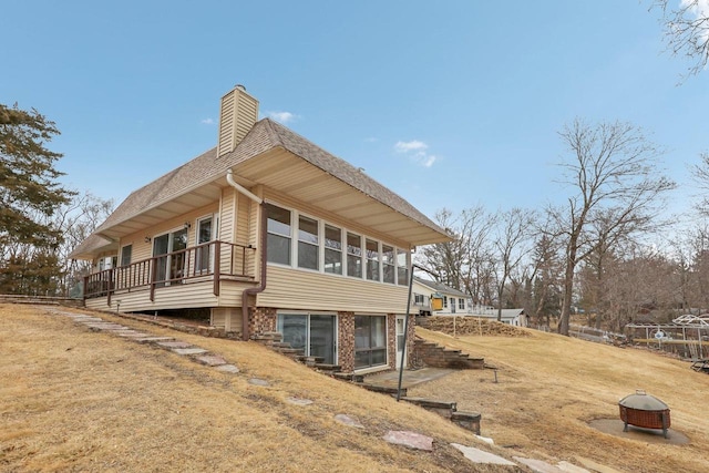 view of side of home with roof with shingles, a chimney, a deck, and a yard