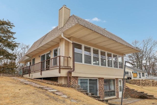 view of home's exterior with a sunroom, a shingled roof, and a chimney