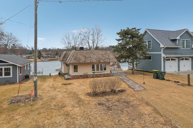 view of front of house featuring a shingled roof, a front lawn, and central AC