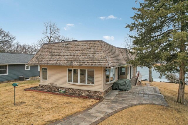 view of front of home with a patio, mansard roof, cooling unit, roof with shingles, and a front yard