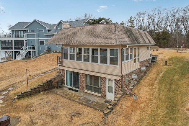 back of house featuring a patio area, roof with shingles, brick siding, and a lawn