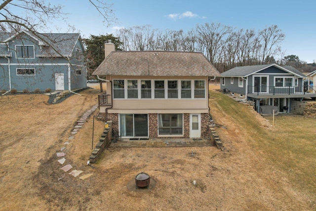 rear view of house with brick siding, a chimney, a shingled roof, a lawn, and stairway