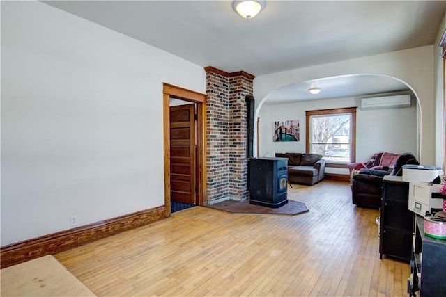 living room with arched walkways, a wall unit AC, baseboards, light wood-style floors, and a wood stove