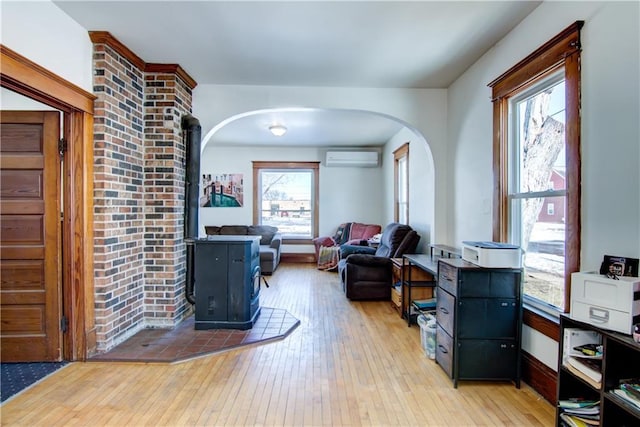 sitting room featuring arched walkways, a wall mounted AC, wood-type flooring, and a wood stove