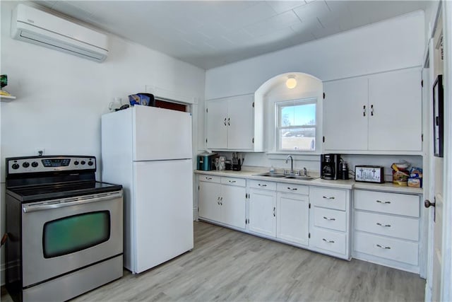 kitchen with a sink, light countertops, stainless steel electric range, freestanding refrigerator, and a wall mounted air conditioner