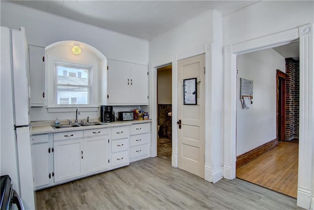 kitchen with white cabinets, light wood-style flooring, freestanding refrigerator, light countertops, and a sink