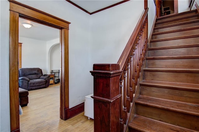 stairs with arched walkways, ornamental molding, wood finished floors, and baseboards