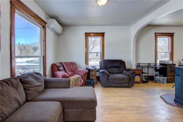 living area featuring arched walkways, light wood finished floors, and a wall mounted AC