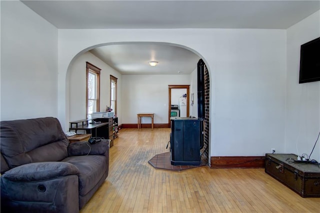 living area featuring light wood-type flooring, arched walkways, and baseboards