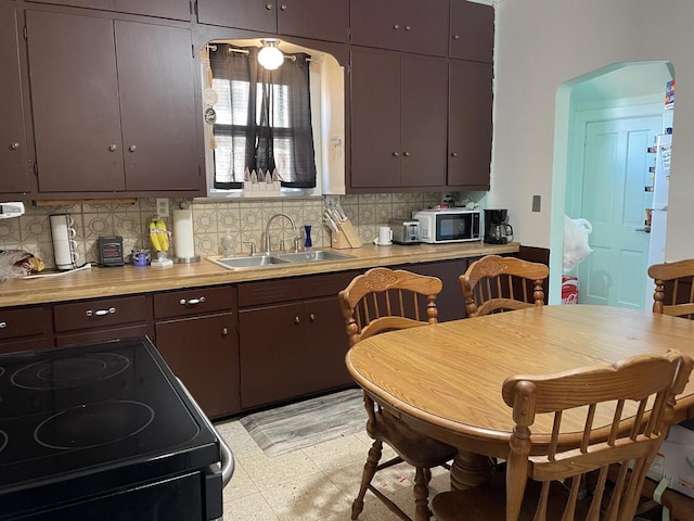 kitchen with tasteful backsplash, arched walkways, black range with electric stovetop, light floors, and a sink