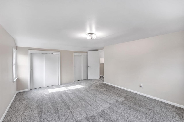 unfurnished bedroom featuring baseboards, two closets, and light colored carpet