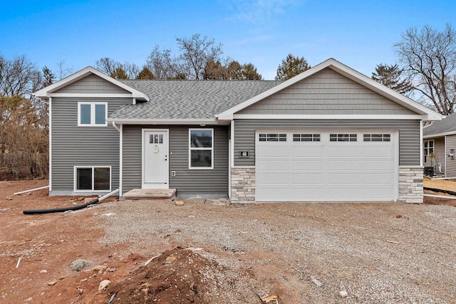 split level home featuring a garage, a shingled roof, and dirt driveway