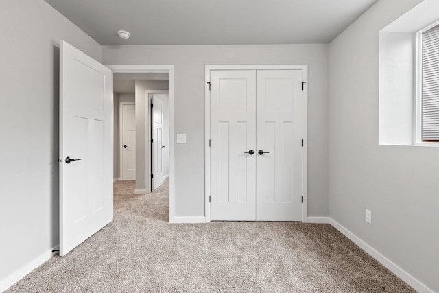 unfurnished bedroom with light carpet, a closet, and baseboards