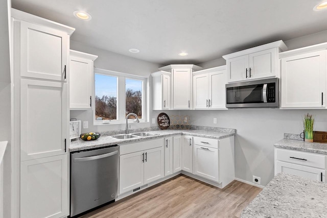 kitchen with stainless steel appliances, white cabinetry, a sink, and light wood finished floors