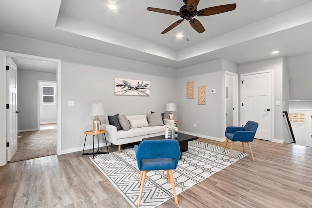 living room featuring light wood-style floors, a tray ceiling, and baseboards