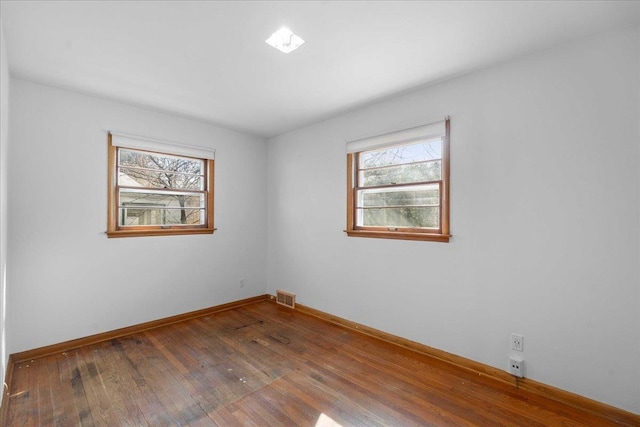 unfurnished room with visible vents, wood-type flooring, and baseboards