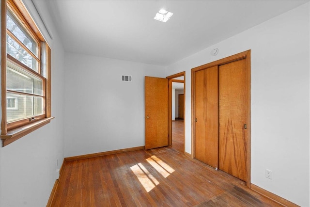 unfurnished bedroom featuring wood finished floors, visible vents, a closet, and baseboards